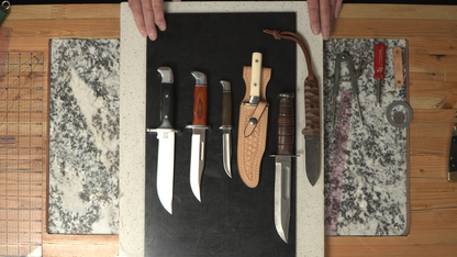 Set of knives displayed on a black mat with leather sheaths.